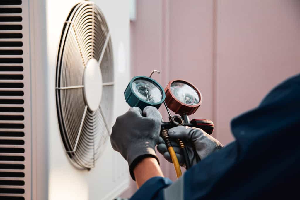 Heat and Air Conditioning, HVAC system service technician using measuring manifold gauge checking refrigerant and filling industrial air conditioner after duct cleaning maintenance outdoor compressor.